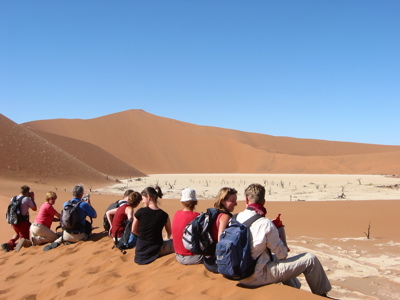 Reizigers rusten op een zandduin met uitzicht op Deadvlei en de rode duinen van Sossusvlei, Namibië.