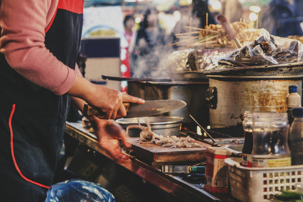 Streetfoodkraam in Zuid-Korea met kok die ingrediënten snijdt en kookt in grote pannen.