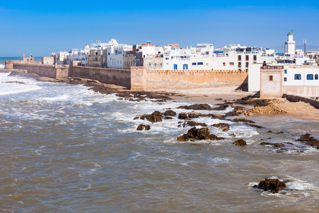 Stadsmuren en witte huizen aan de kust van Essaouira, Marokko, met golven en rotsen in zee.