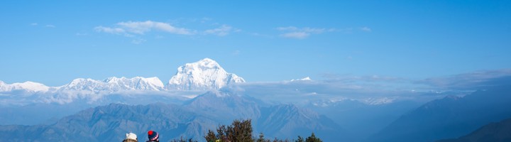 Uitzicht vanaf Poon Hill met gebedsvlaggen en trekkers, met besneeuwde Himalaya-toppen op de achtergrond.