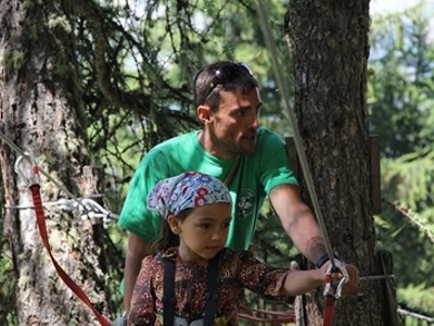 Kind in klimharnas op een touwenparcours in het bos, begeleid door een instructeur in de Écrins, Frankrijk.