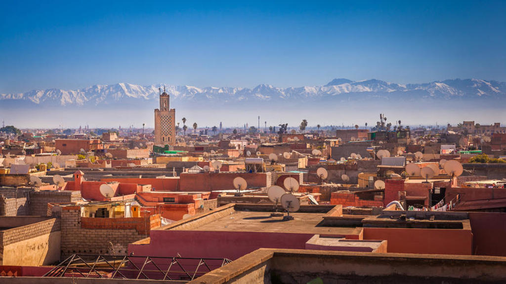 Uitzicht over de daken van Marrakech met minaret en het Atlasgebergte op de achtergrond.