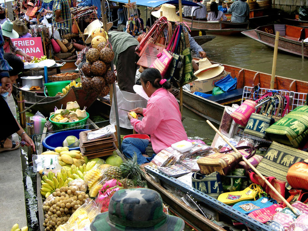 Drukke drijvende markt in Thailand met boten vol fruit, snacks en kleurrijke souvenirs.