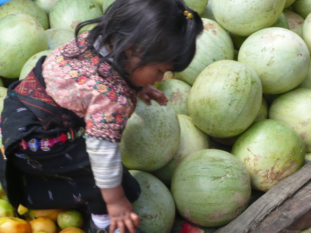 Kind tussen grote meloenen op een markt in Guatemala tijdens een groepsrondreis.