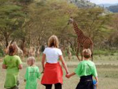Gezin wandelt door een wildpark in Kenia met giraffe op de achtergrond.