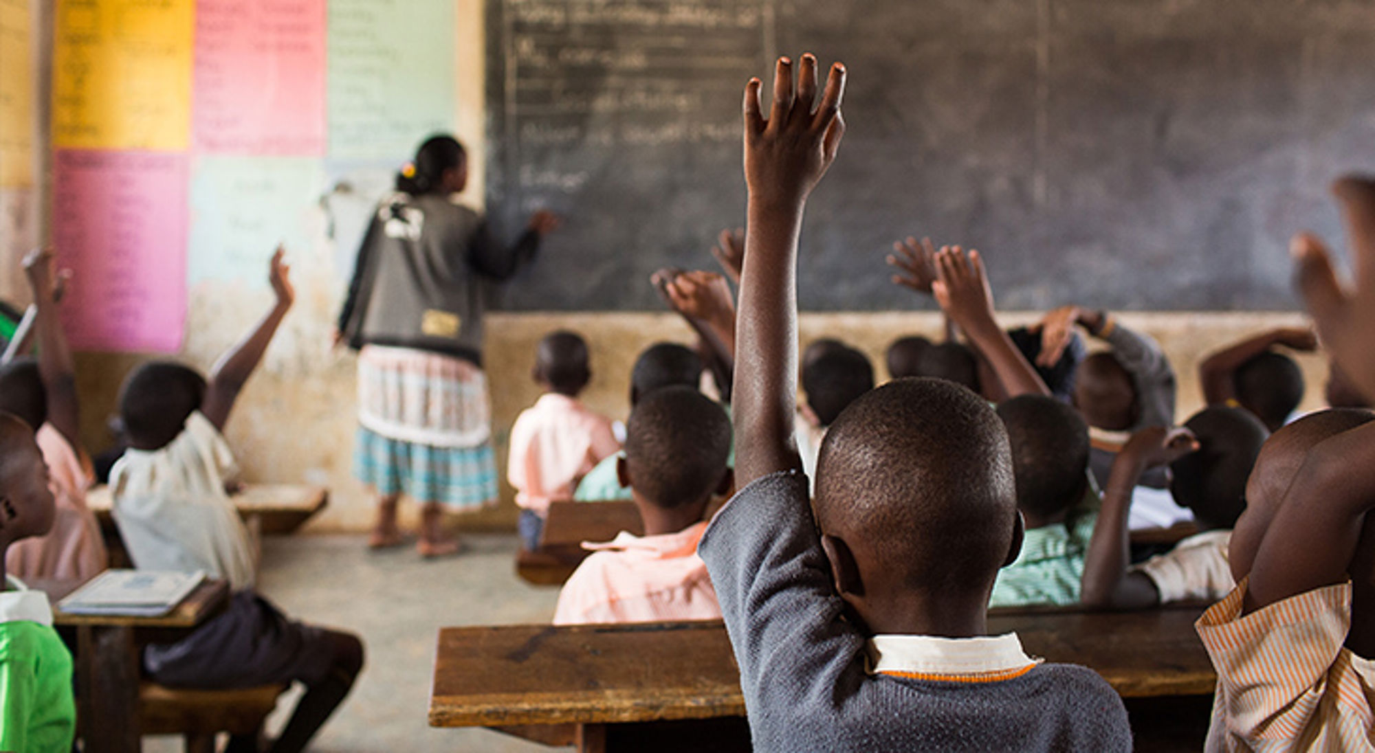 Bezoek geen scholen Kinderen in een klaslokaal steken hun hand op terwijl de docent lesgeeft voor het schoolbord.