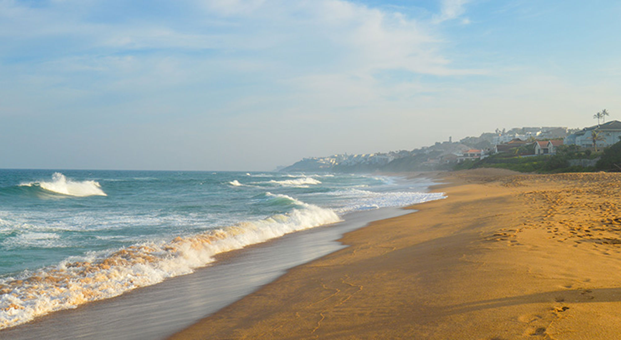Strand van Durban Zandstrand met golven langs de kust in Zuid-Afrika, met huizen op de heuvel in de verte.