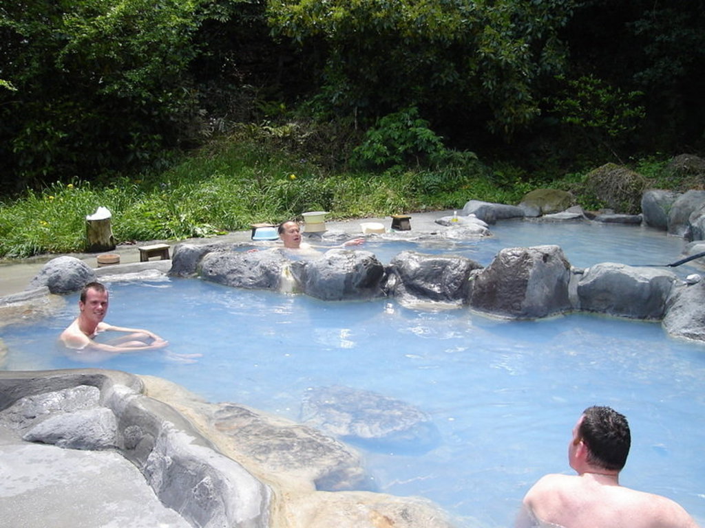 Reizigers ontspannen in een Japanse onsen tussen rotsen en groen tijdens groepsrondreis Japan Hoogtepunten.
