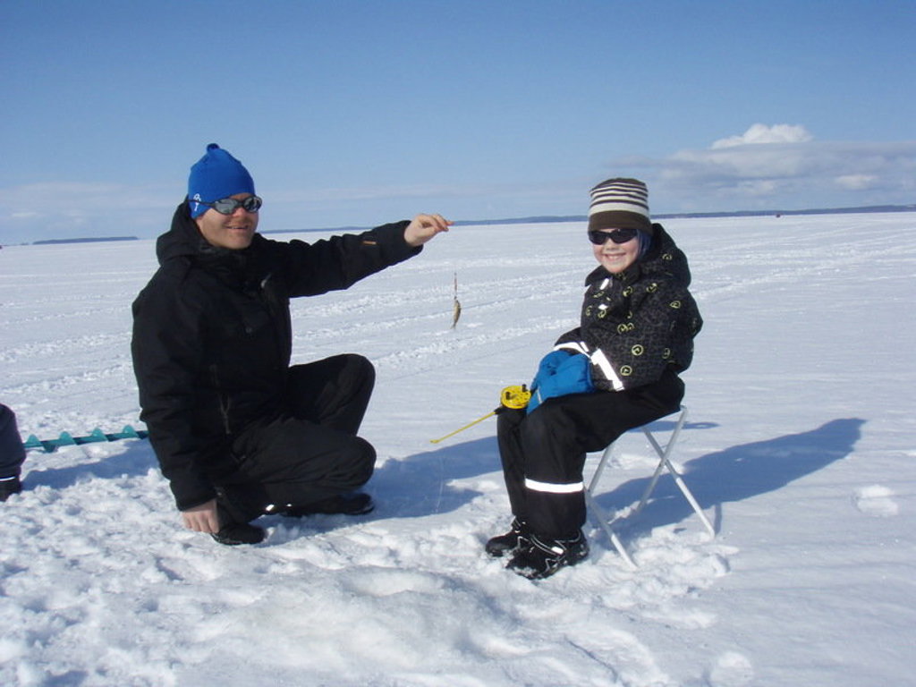 Vader en kind ijsvissen op een bevroren meer in Lapland tijdens familiereis in de winter.