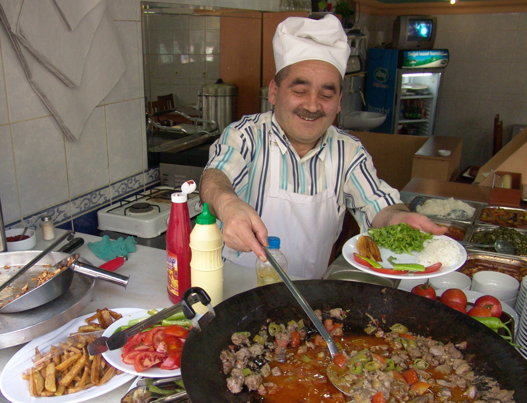 Turkse kok schept vers bereide maaltijd op in een lokaal restaurant aan de Turquoise Kust tijdens familiereis Turkije.