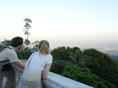 Twee reizigers kijken vanaf Doi Suthep uit over Chiang Mai en de groene heuvels in Thailand.