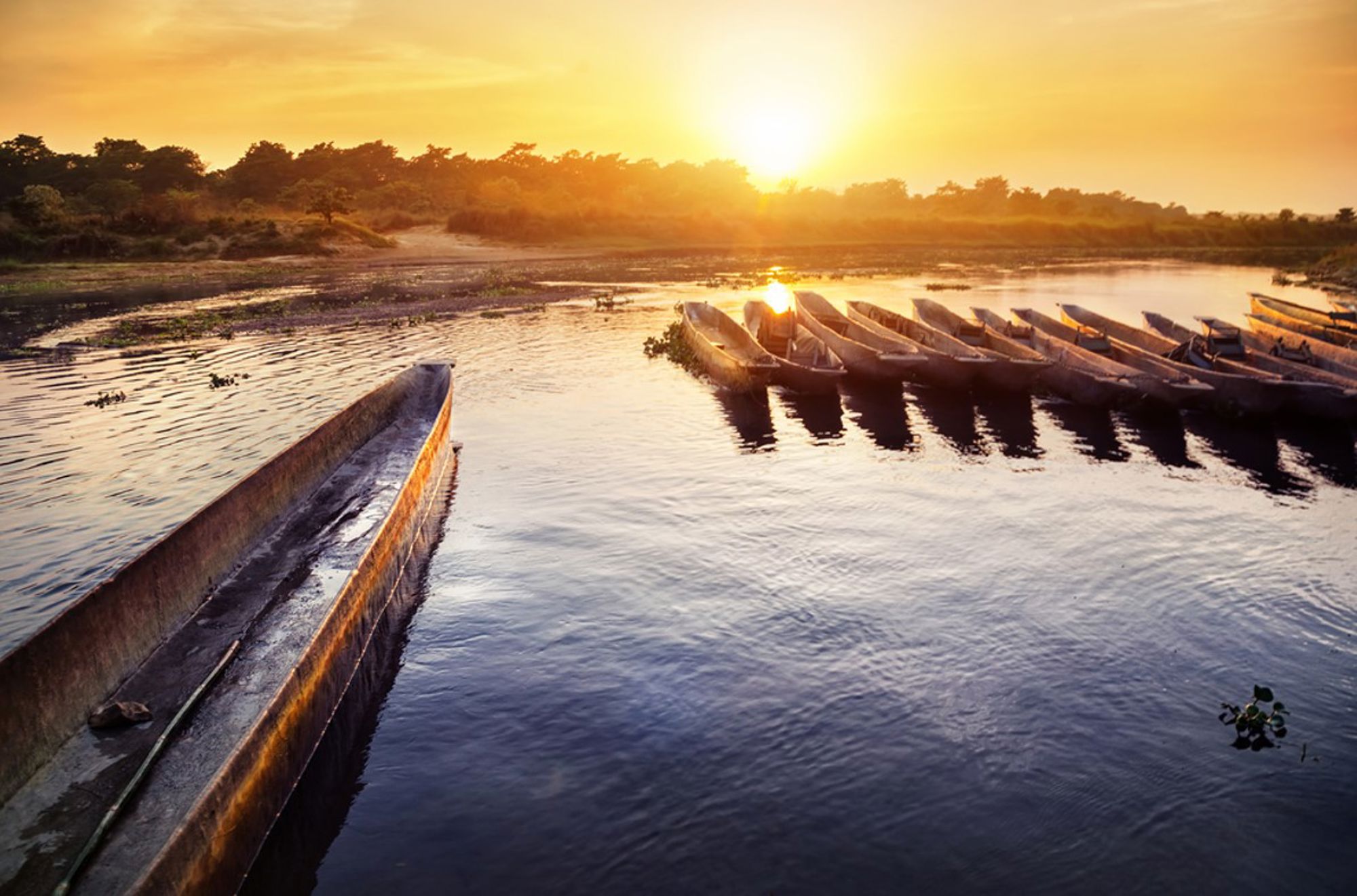Houten kano’s aan de oever van een rivier bij zonsondergang in Nepal.