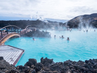 Badende mensen in de Blue Lagoon met stoom boven het turquoise geothermische water en houten bruggen.