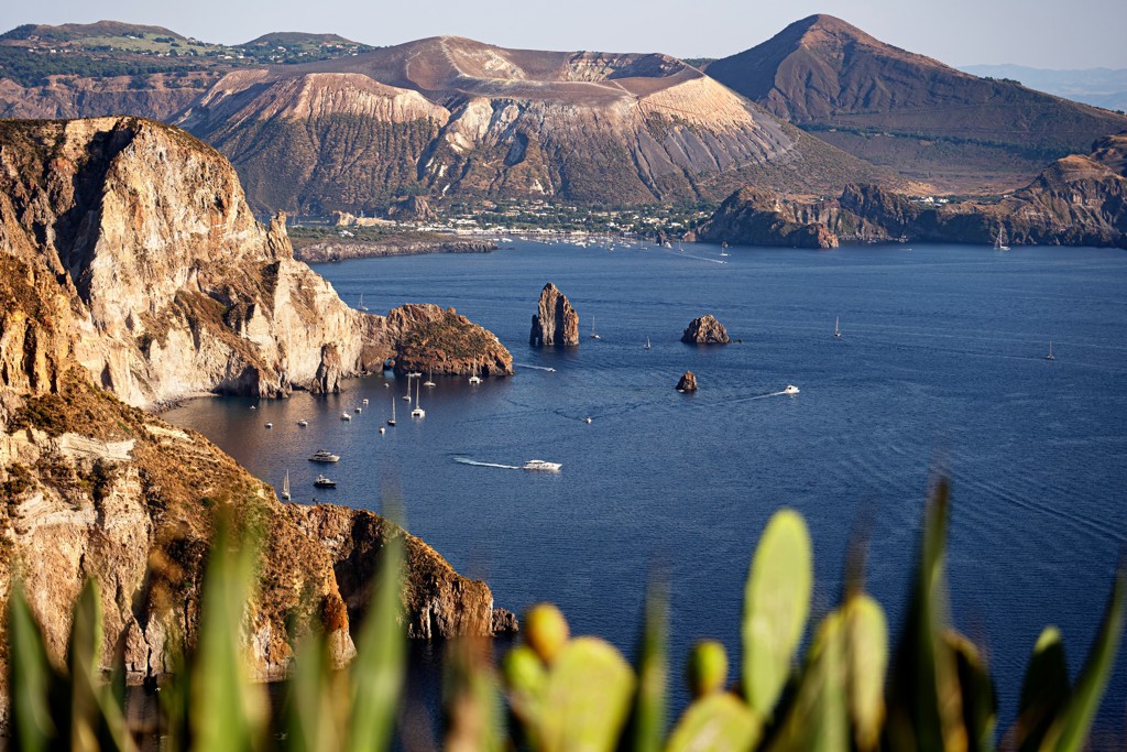Uitzicht op de kust van Sicilië met vulkanische bergen en zeilboten bij de Eolische Eilanden.