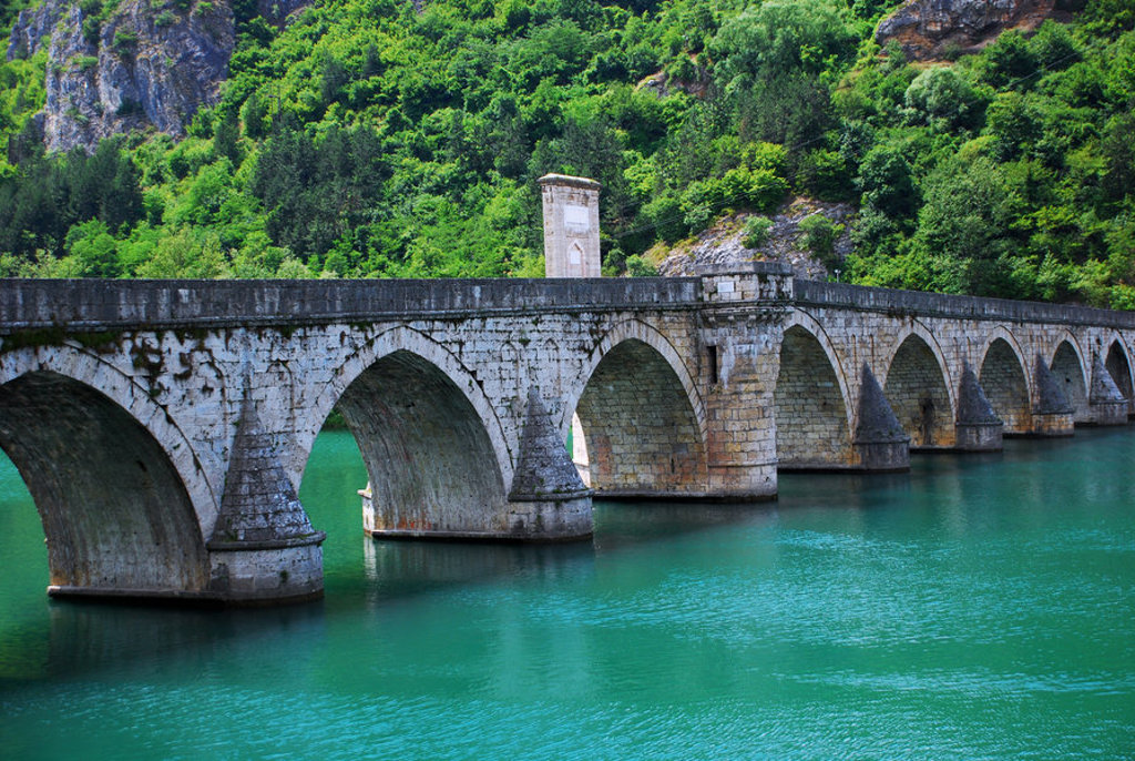 Oude stenen boogbrug over een turquoise rivier, omringd door groene heuvels tijdens een groepsrondreis Balkan.