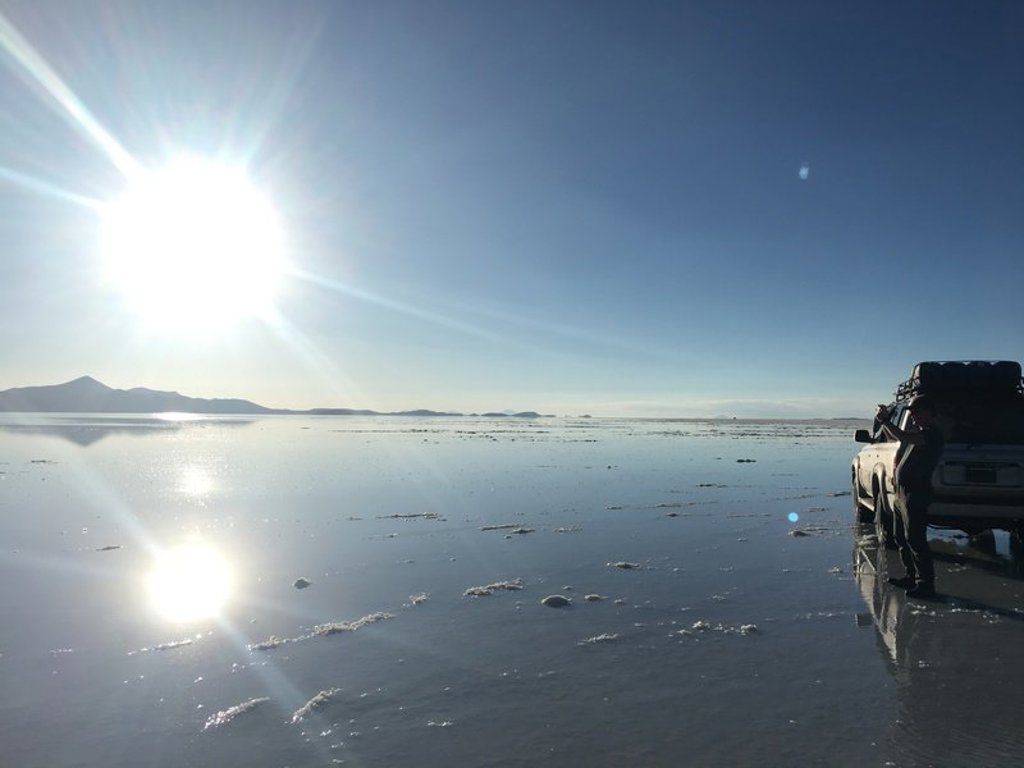 4x4-auto op de zoutvlakte Salar de Uyuni in Bolivia, met spiegeling van de zon in het water.