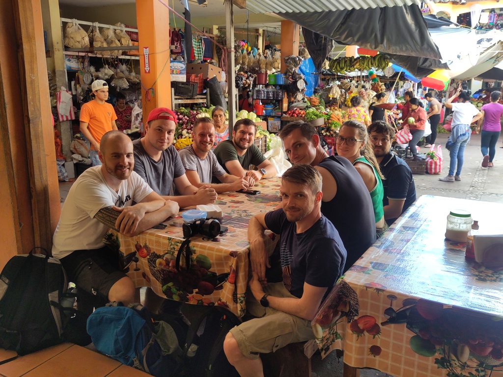 22-35ers groepsreis: reizigers aan tafel op een kleurrijke markt met groente- en fruitkramen in Guatemala.