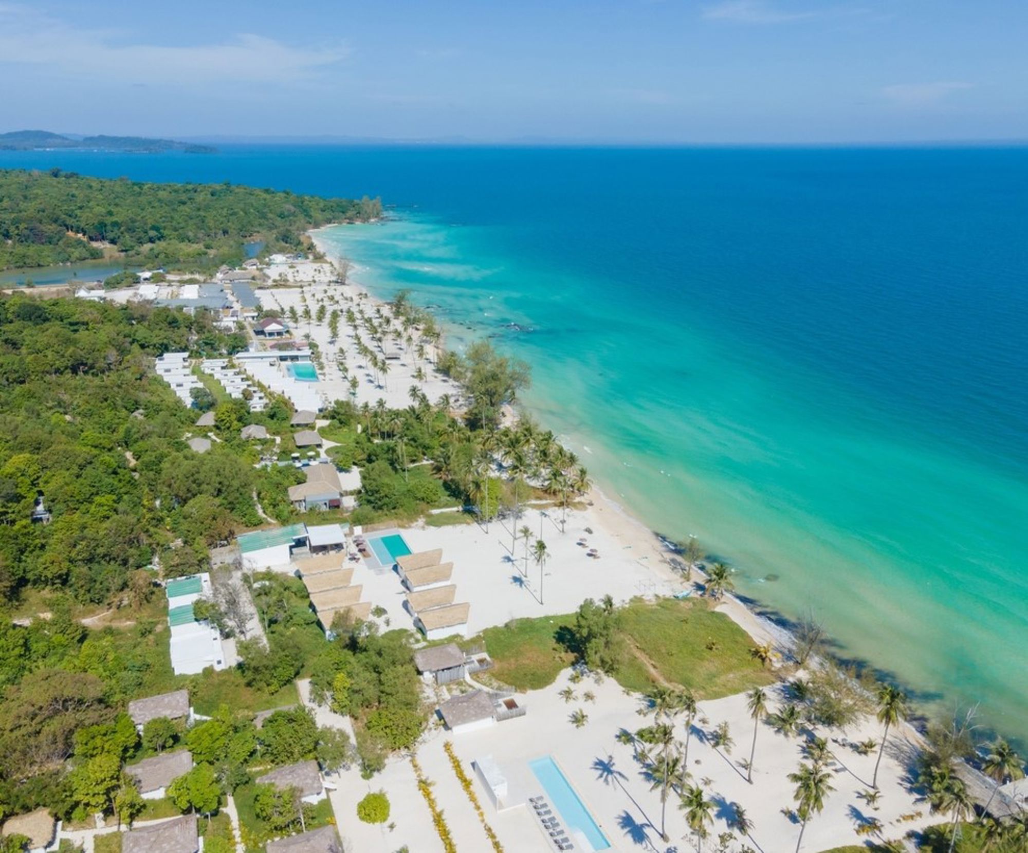een wit zandstrand met palmbomen en helderblauwe zee in Cambodja.