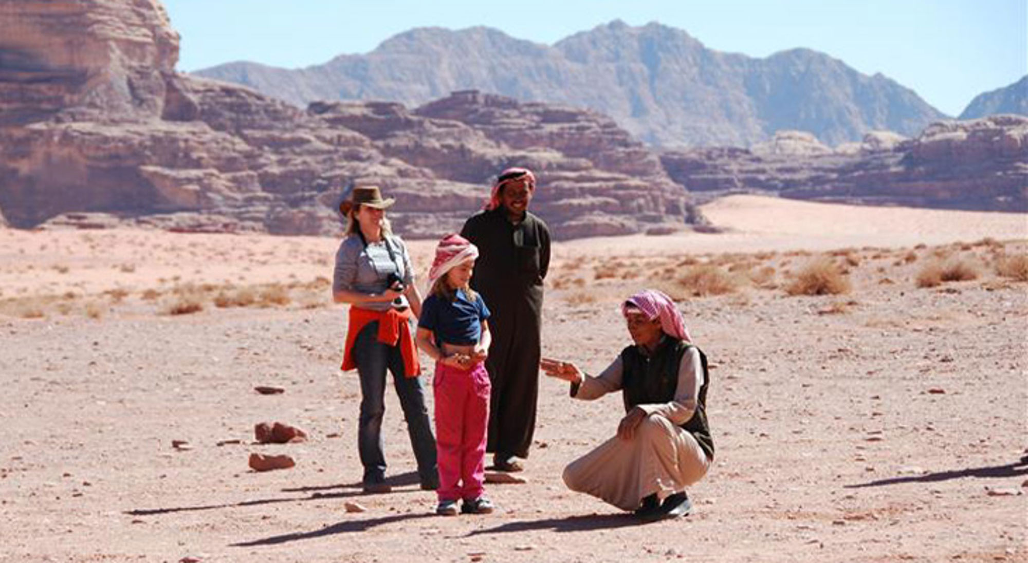 Ontmoeting Jordanië Gezin met lokale gids in de Wadi Rum-woestijn, Jordanië, met rotsformaties op de achtergrond.