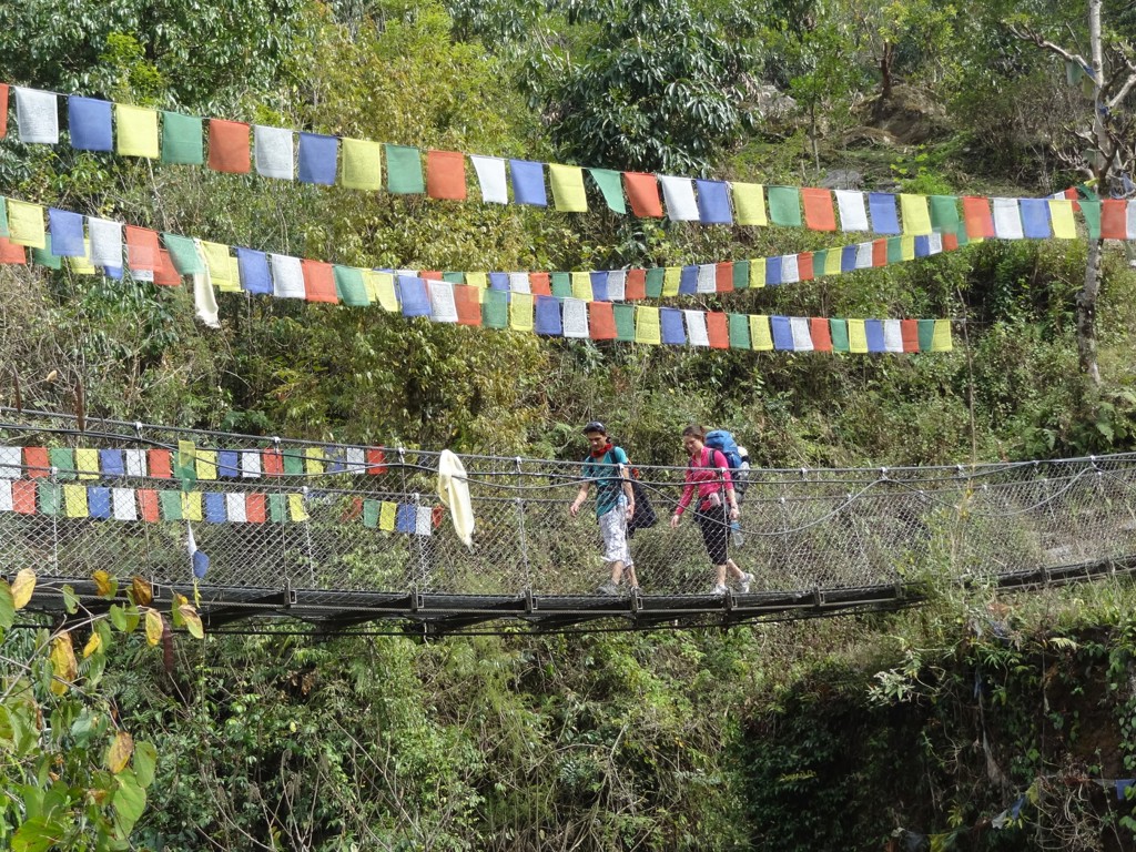 Wandelaars steken een hangbrug met gebedsvlaggen over tijdens een familiereis in Nepal.