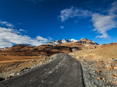 Eenzame bergweg door het ruige landschap van Spiti & Ladakh, met besneeuwde toppen onder een blauwe lucht.
