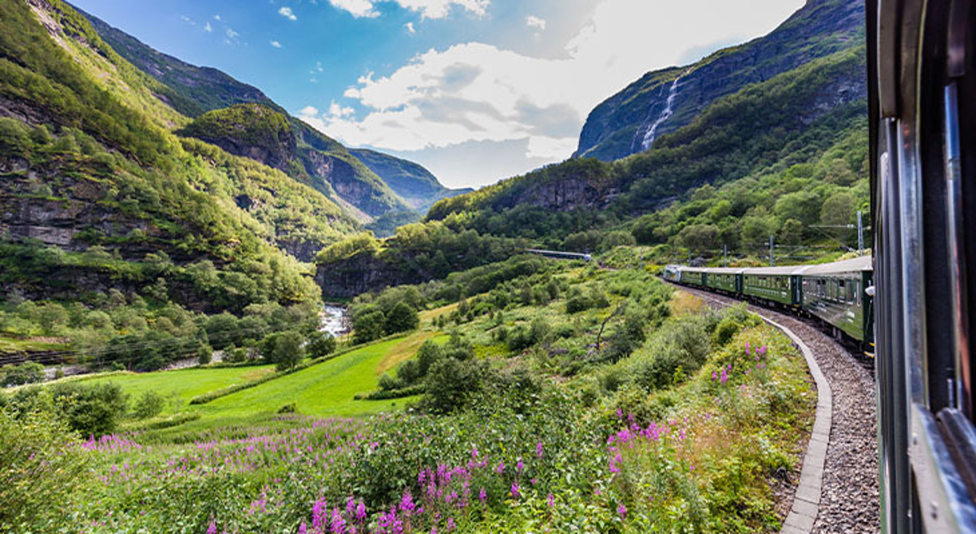 Flamsbana treinreis Groene trein door een bergvallei met rivier en waterval, gezien vanuit het raam.
