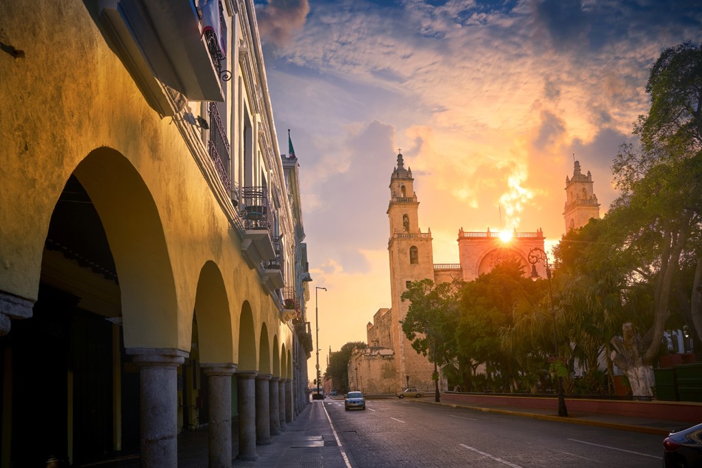 Historisch straatbeeld in Mérida, Mexico, met koloniale bogen en kathedraal bij zonsondergang.