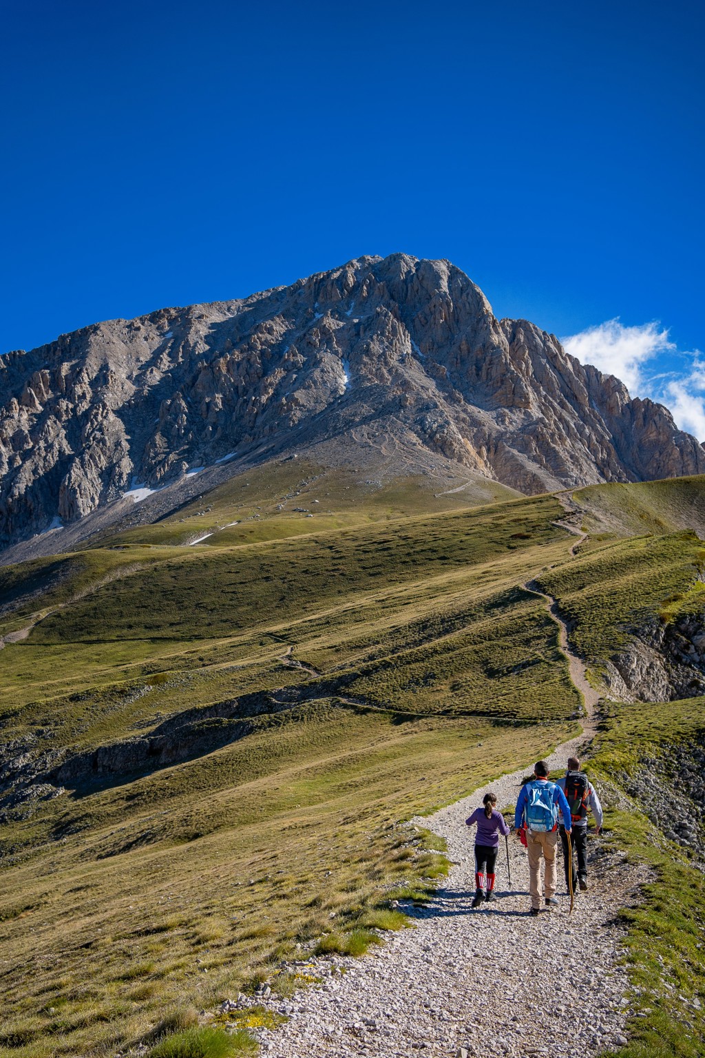 Wandelaars op bergpad in de Centrale Apennijnen, Italië, met rotsmassief onder heldere blauwe lucht.