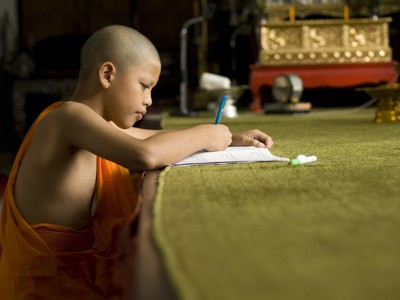 Jonge boeddhistische monnik schrijft in een schrift in een tempel in Thailand.