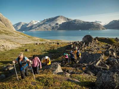 Wandelaars tijdens een bergtocht langs een fjord met rotsen en gletsjers op de achtergrond.