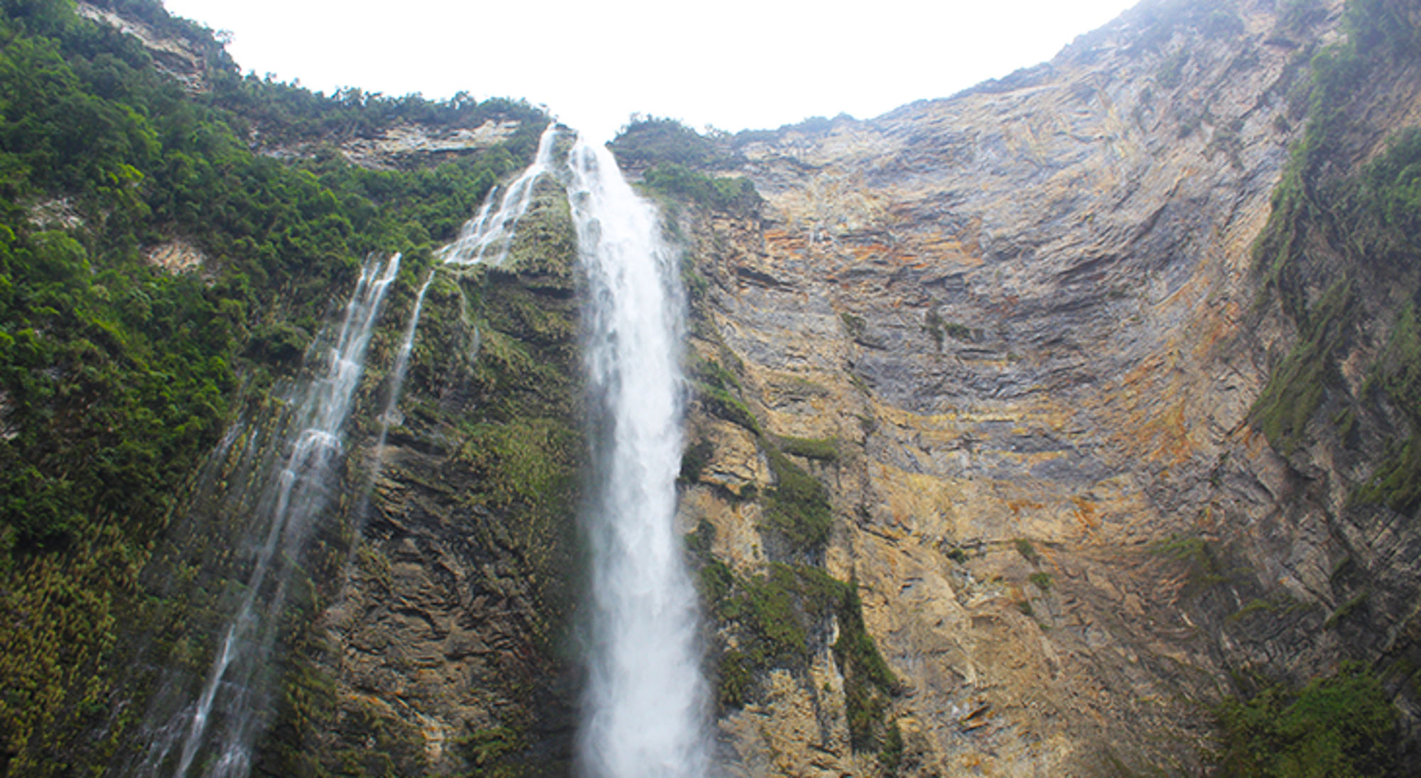 Hoge waterval langs een steile rotswand, omringd door groen.