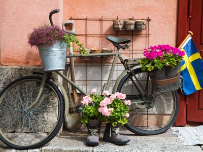 Fiets met bloemenmanden en Zweedse vlag bij een kleurrijke gevel in Scandinavië.