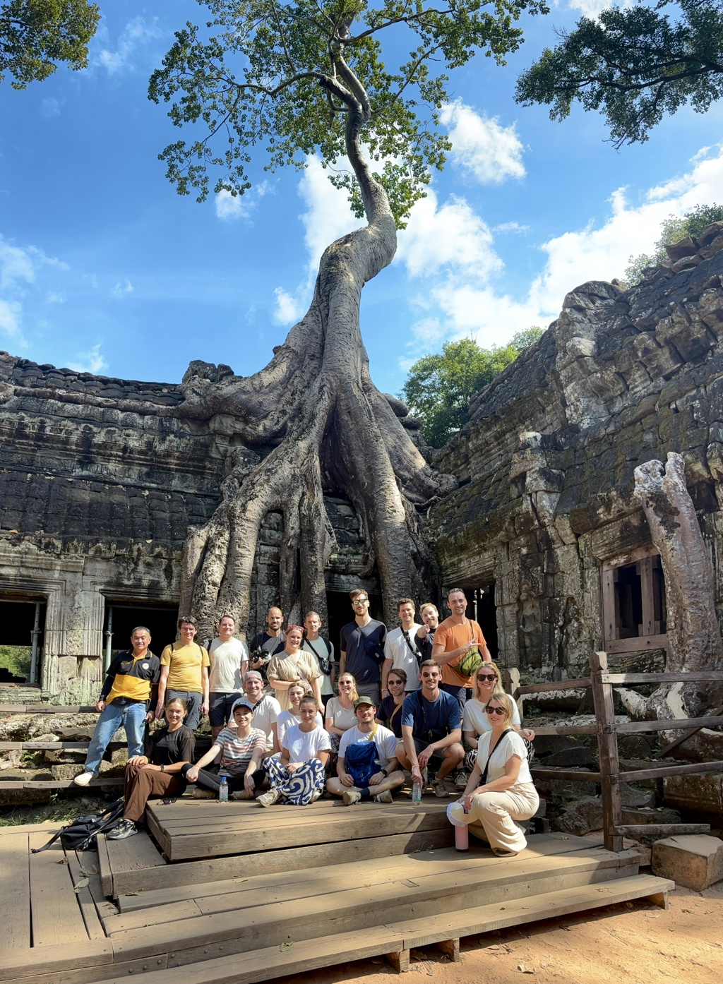 Groepsfoto van 22-35ers bij Angkor-tempel met enorme boomwortels in Cambodja.