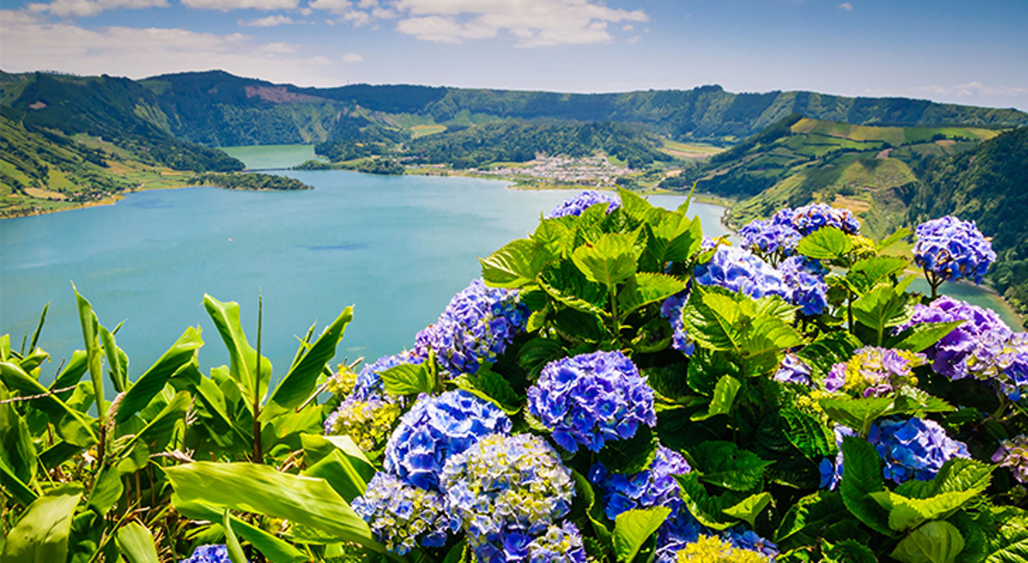 Uitzicht op een kratermeer met groene heuvels en bloeiende hortensia’s tijdens een wandelvakantie met Sawadee.