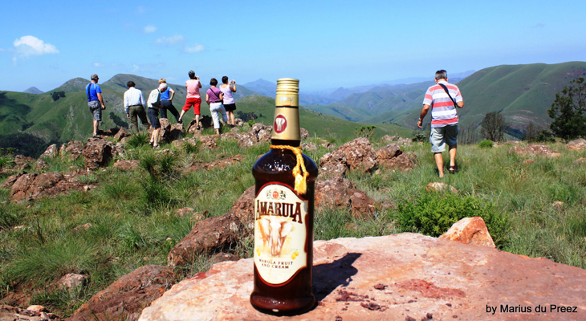 Amarula in zuid afrika Fles Amarula op een rots met wandelaars en uitzicht op groene bergen.