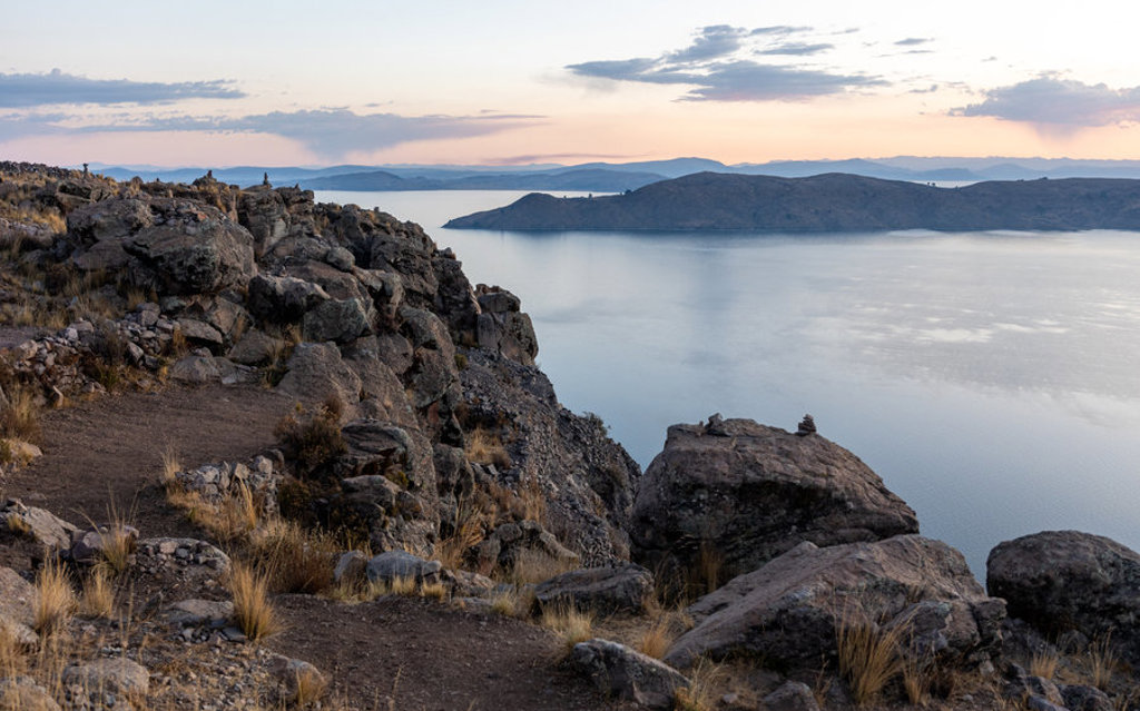 Zonsondergang bij het Titicacameer in Peru, met rotsachtige oever en eilanden op de achtergrond.