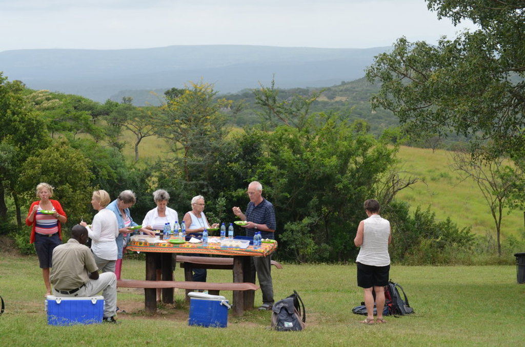 Reizigers lunchen tijdens een groepsrondreis in Noordelijk Zuid-Afrika en eSwatini, met uitzicht op groen heuvelgebied.