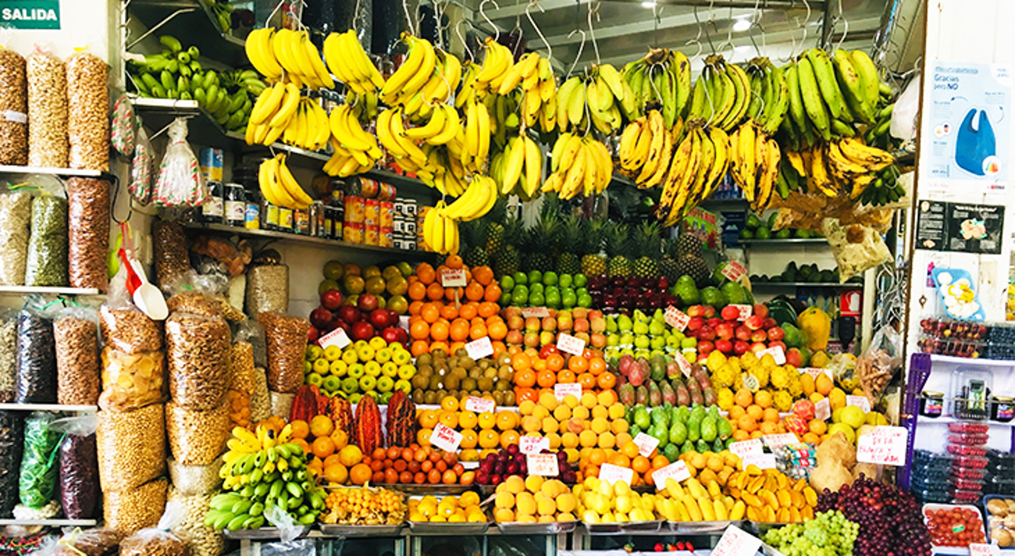 Kleurrijke fruitkraam op een markt met hangende bananen en stapels citrus, ananas en druiven.