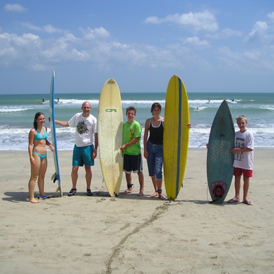 Gezin met surfplanken op het strand van Bali tijdens familiereis Java en Bali.