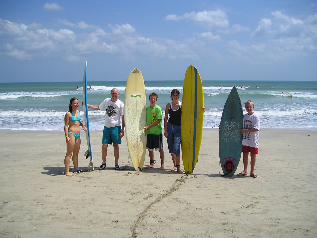 Gezin met surfplanken op het strand van Bali tijdens familiereis Java en Bali.