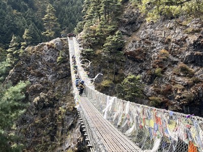 Wandelaars op hangbrug met gebedsvlaggen tijdens de Route Nepal Everest Base Camp-trektocht.