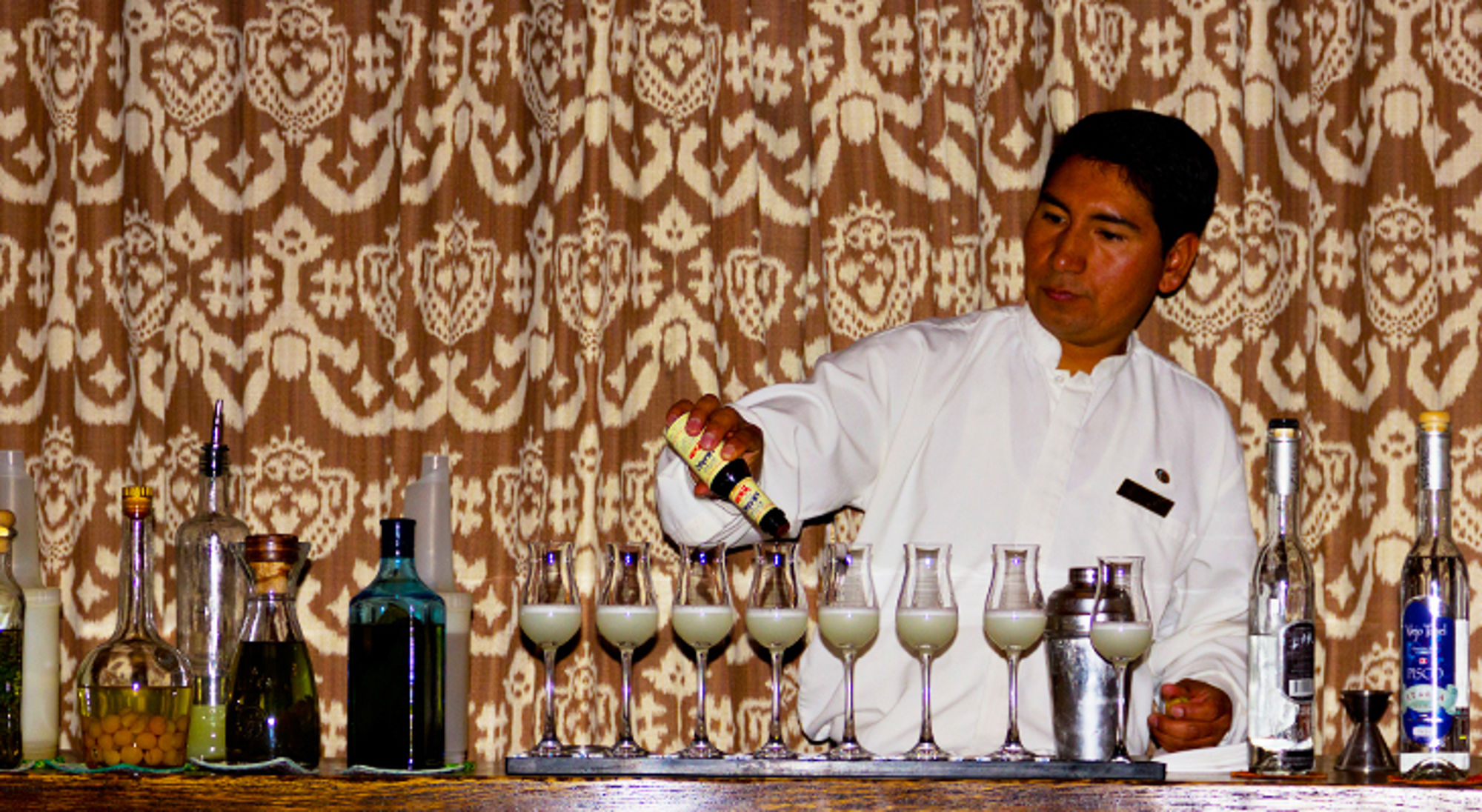 barman in Peru Barman schenkt een cocktail in meerdere glazen aan de bar, met flessen en cocktailshaker op de achtergrond.