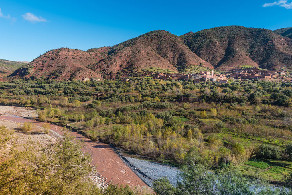 Groene vallei met rivier en dorp aan de voet van het Atlasgebergte in Marokko.