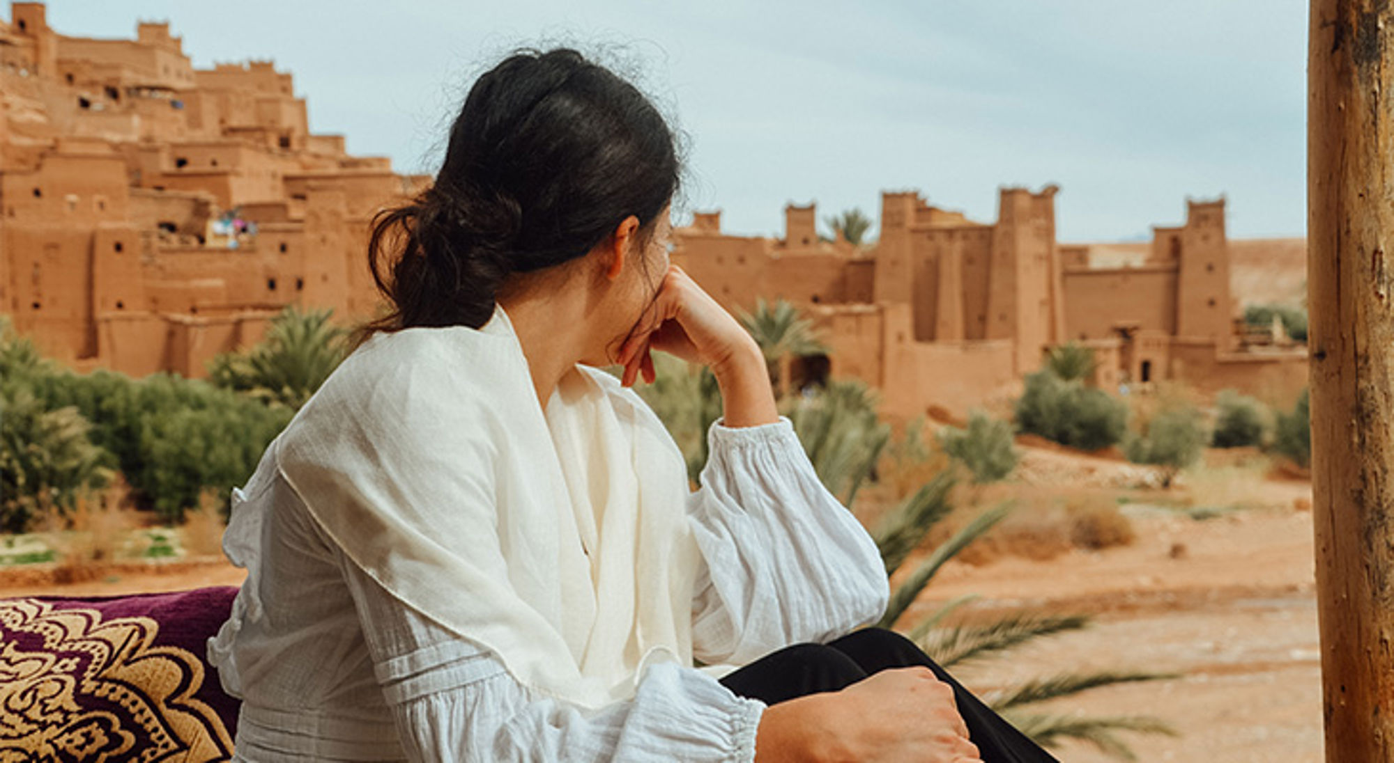 Uitzichtpunt Aït-Ben-Haddou Vrouw kijkt uit over een traditionele lemen kasbah met palmbomen in de woestijn.