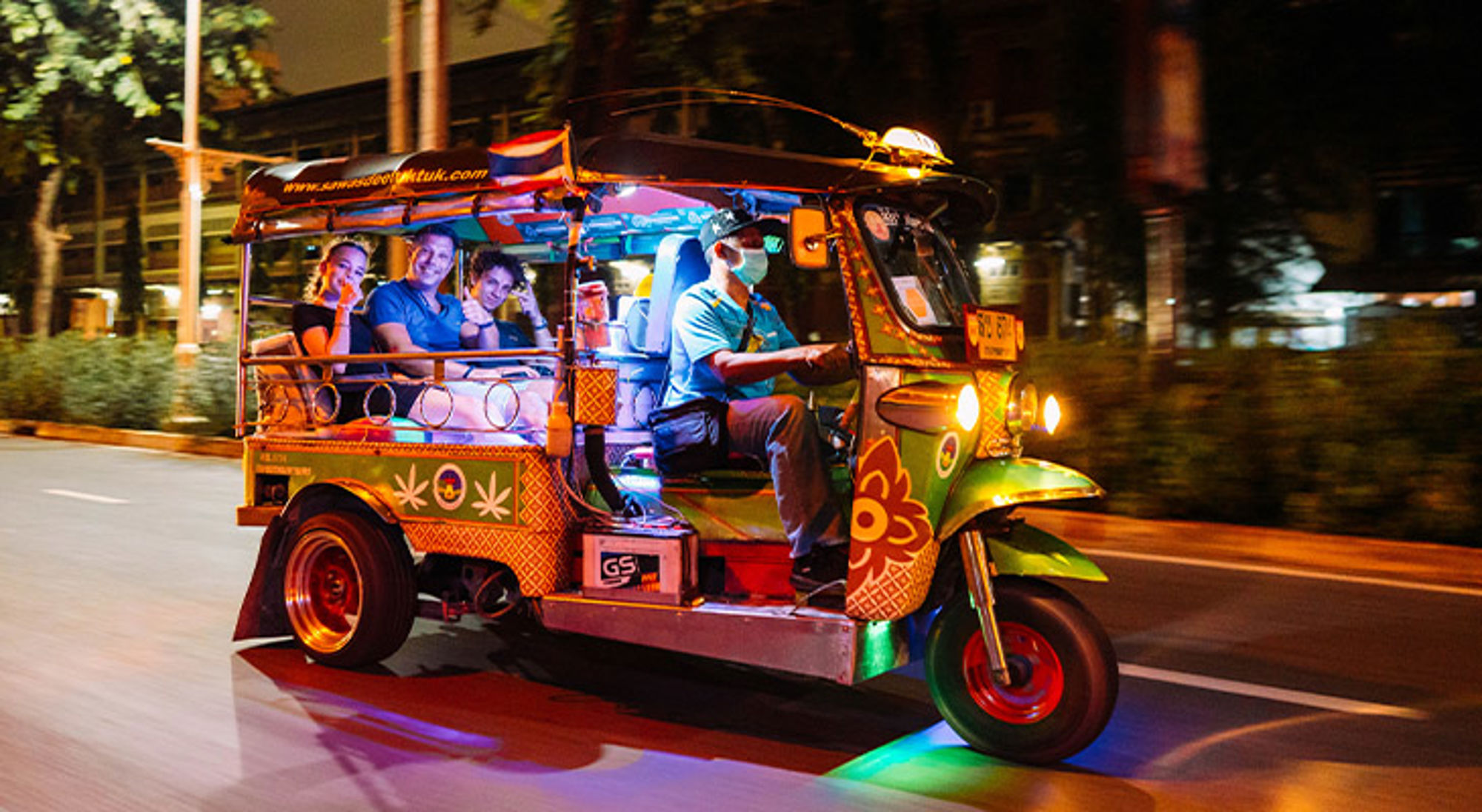 Kleurrijke tuk-tuk met passagiers rijdt ’s avonds door de stad.