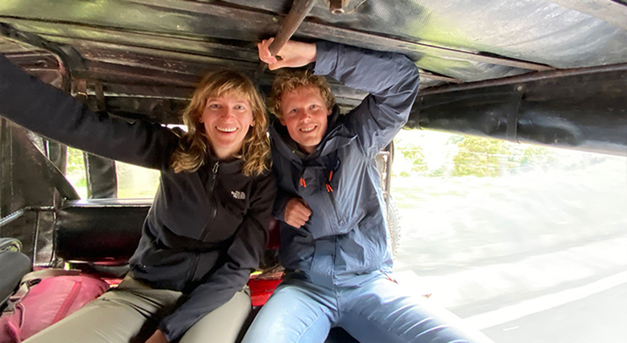 Jasper en Marianne in Colombia Twee reizigers in de achterbak van een rijdende jeep, lachend en zich vasthoudend aan het dak.