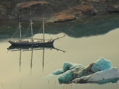 Zeilschip Antigua bij Spitsbergen met drijvende ijsberg in rustig water.