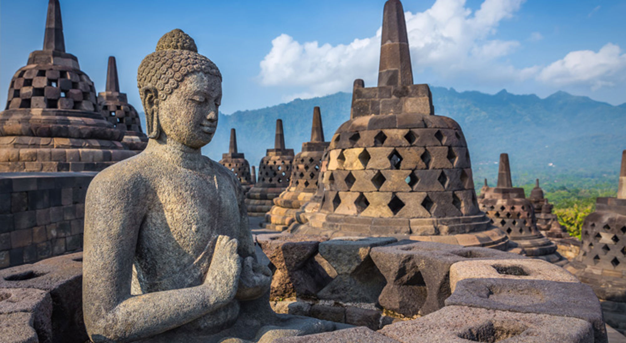 Boeddhabeeld bij de Borobudur-tempel op Java, Indonesië, met stupa’s en bergen op de achtergrond.