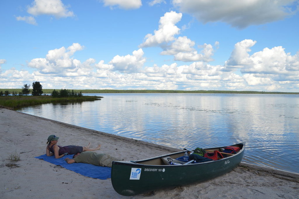 Kanotocht in zomers Lapland, Finland: kano op het strand bij een rustig meer onder een blauwe lucht met wolken.