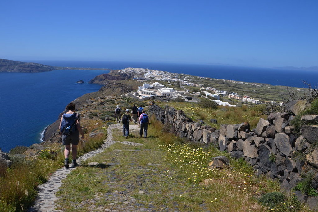 Wandelaars op kustpad met uitzicht op zee en witte dorpen op Santorini, tijdens wandelvakantie Griekenland.